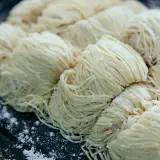 Surowe, cienkie nitki makaronu ułożone w porcje na ciemnej tacy. Czy pies może jeść makaron?