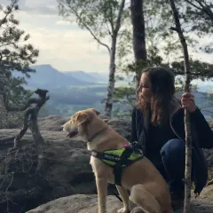Pies i jego opiekunka podczas dog trekking w górach. Pies w kamizelce Julius-K9 patrzy w dal.