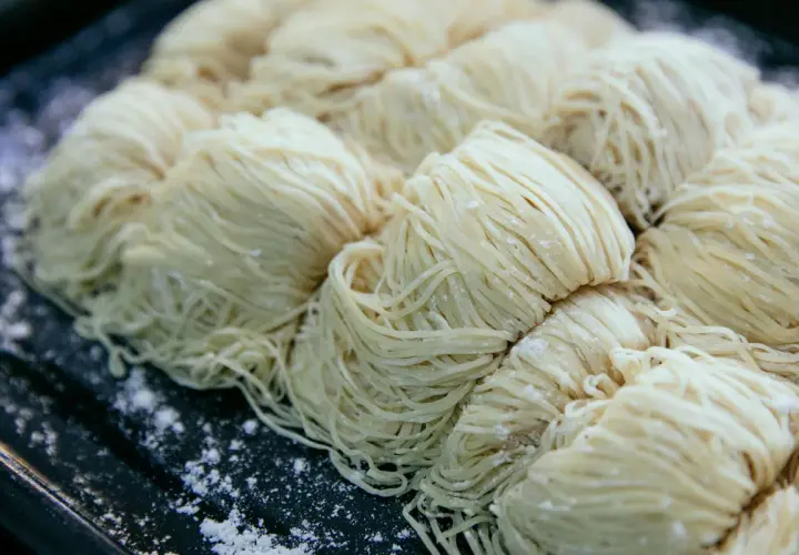 Surowe, cienkie nitki makaronu ułożone w porcje na ciemnej tacy. Czy pies może jeść makaron?