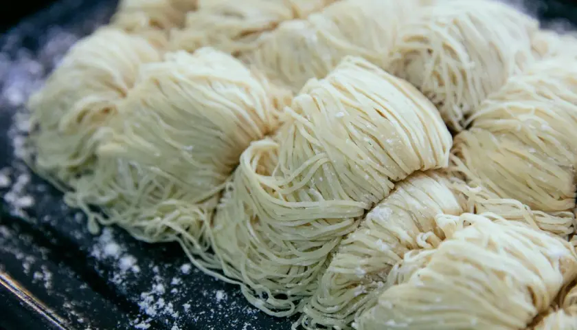 Surowe, cienkie nitki makaronu ułożone w porcje na ciemnej tacy. Czy pies może jeść makaron?