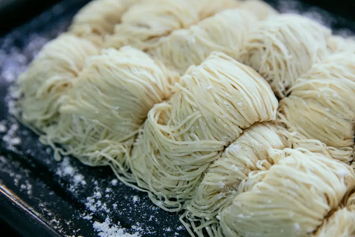 Surowe, cienkie nitki makaronu ułożone w porcje na ciemnej tacy. Czy pies może jeść makaron?