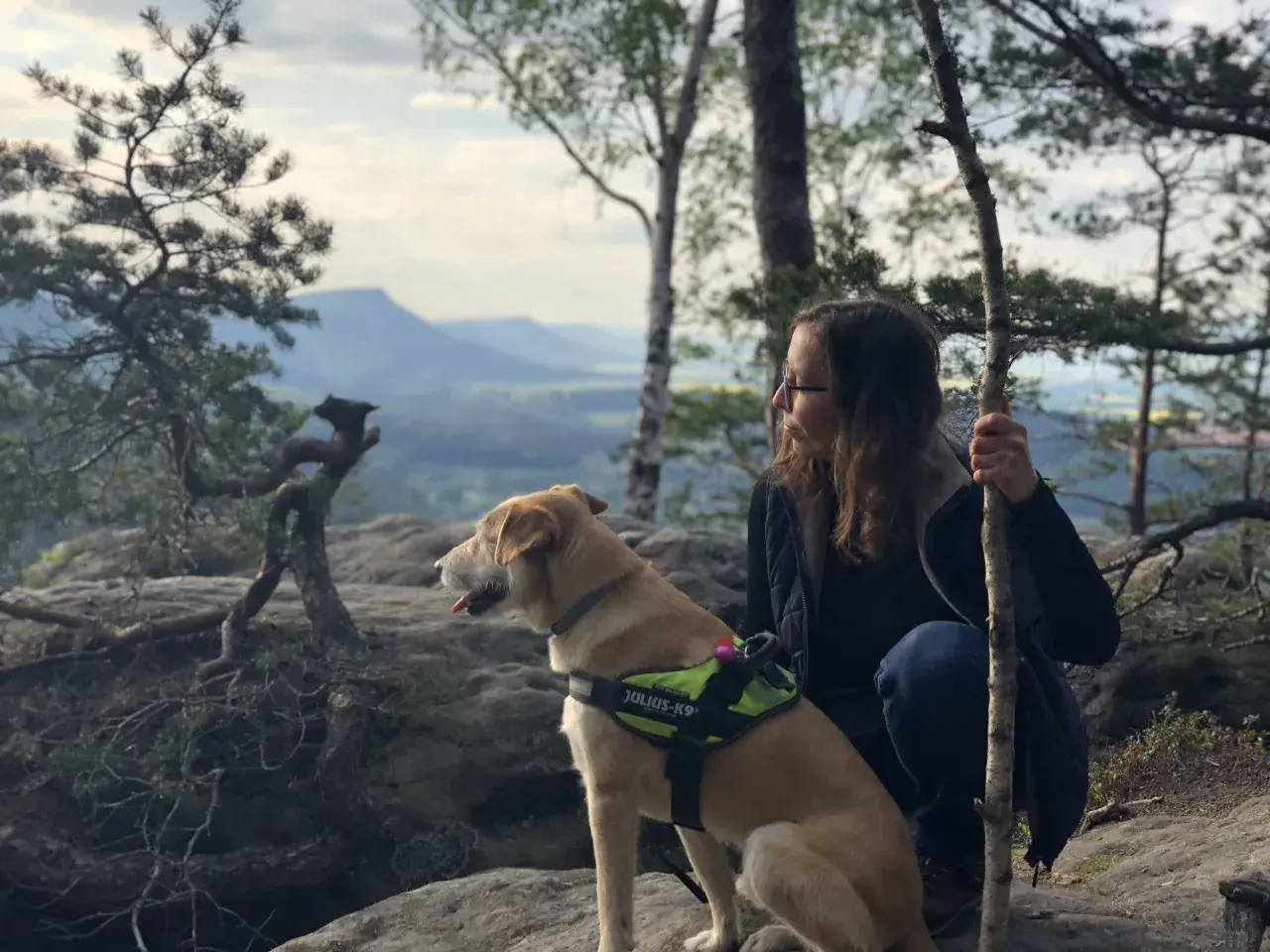 Pies i jego opiekunka podczas dog trekking w górach. Pies w kamizelce Julius-K9 patrzy w dal.